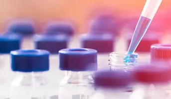 Pippete droping blue liquid being into single small glass bottle