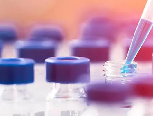 Pippete droping blue liquid being into single small glass bottle